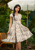 A woman wears a cream cotton woodland animals greta wrap dress with pockets featuring a v-neck and gathered waistband