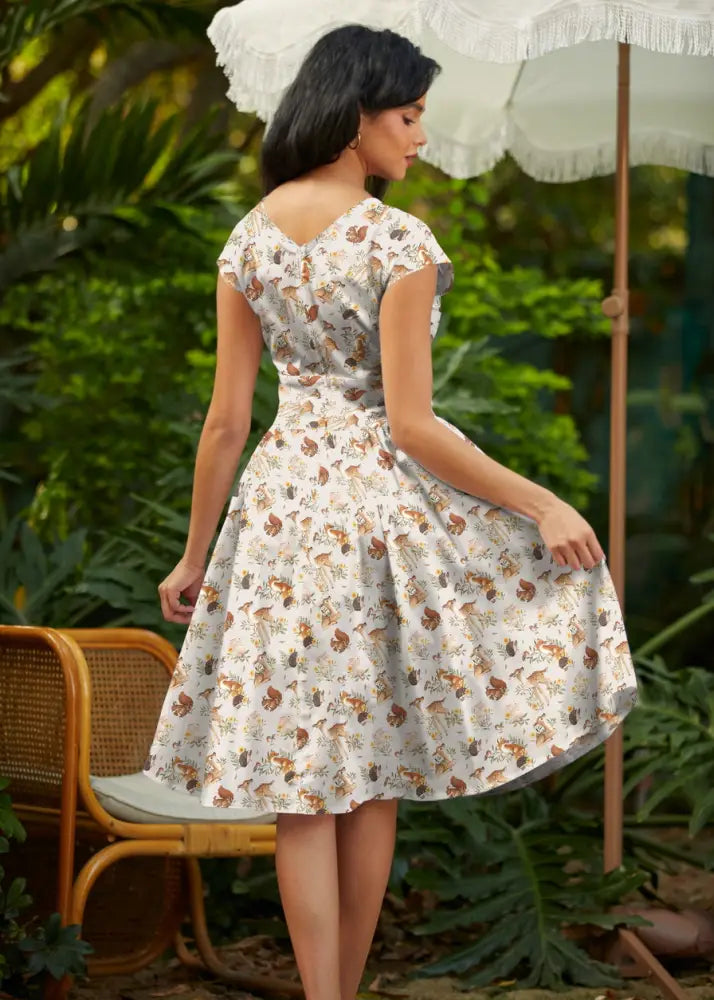 A woman wears a white cotton woodland animals Greta wrap dress with pockets and a brown and green creature pattern