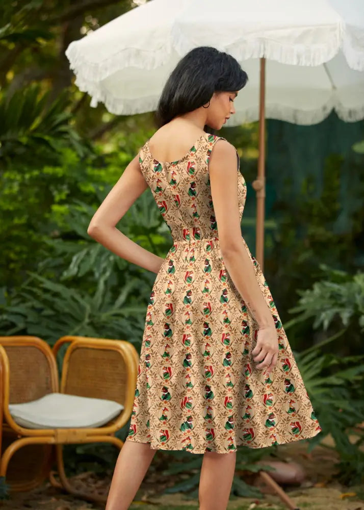 A woman wears a beige sleeveless vintage cotton fit and flare dress with colorful bird patterns woodland scout style
