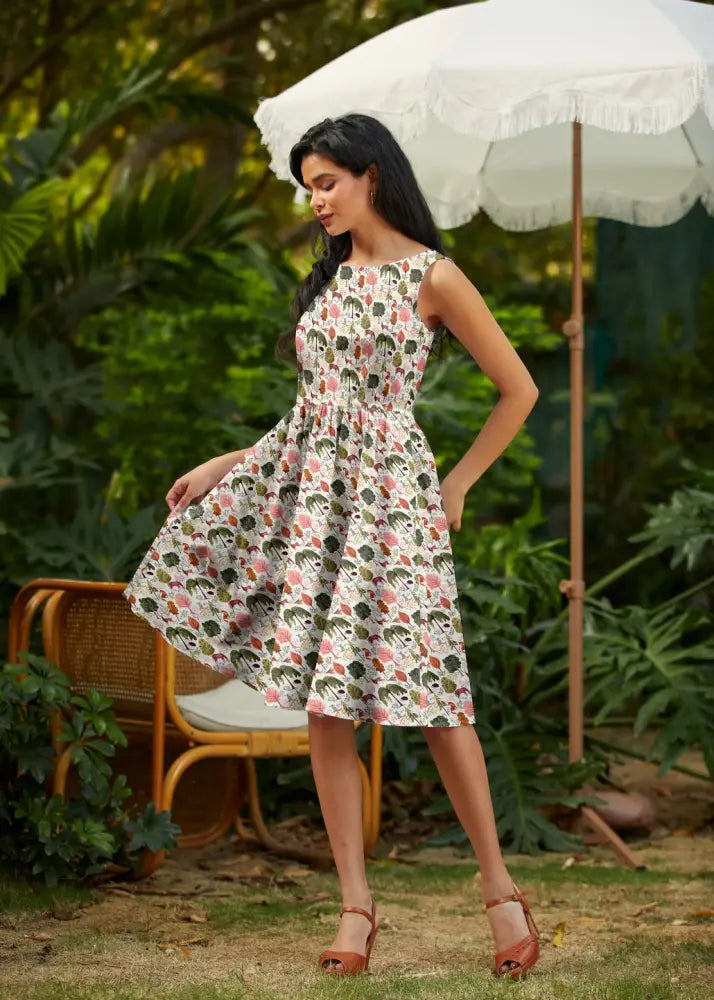 A woman wears a sleeveless woodland vintage cream cotton a-line dress with pockets and a pink green skull pattern