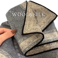 A sophisticated gray and cream paisley wool silk pocket square with a contrasting black border for formal wear