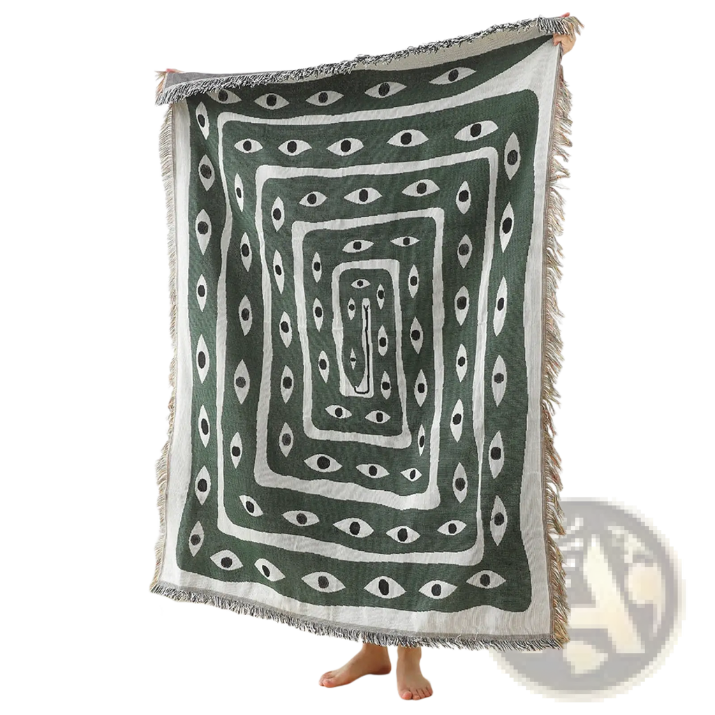 A dark green woven cotton throw blanket with white geometric concentric rectangles and eye motifs, fringed edges