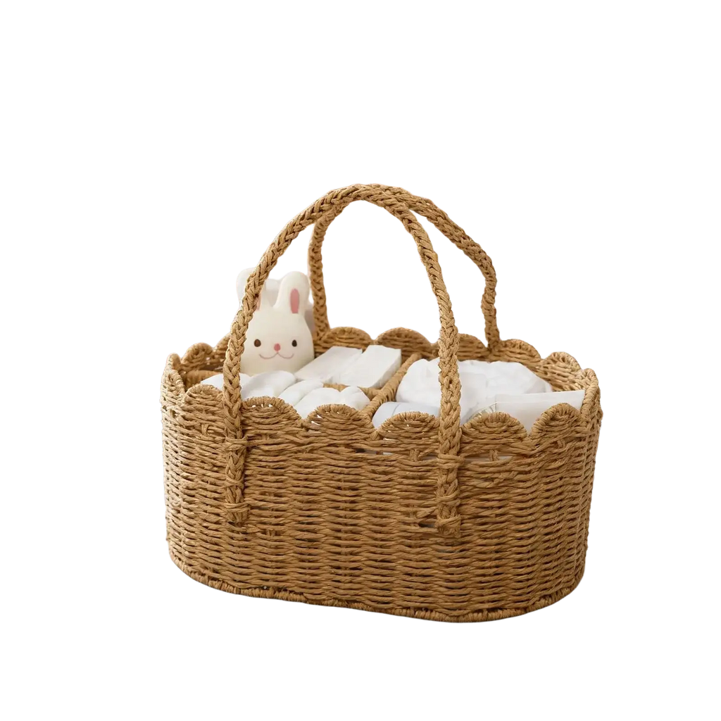 Woven diaper caddy made of natural rattan with scalloped edges and braided handles filled with white linens and plush bunny
