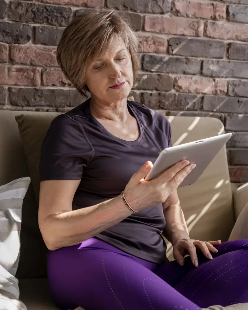 A sleek silver tablet held in a woman’s hands showcasing the woven copper magnetic therapy bangle bracelet product