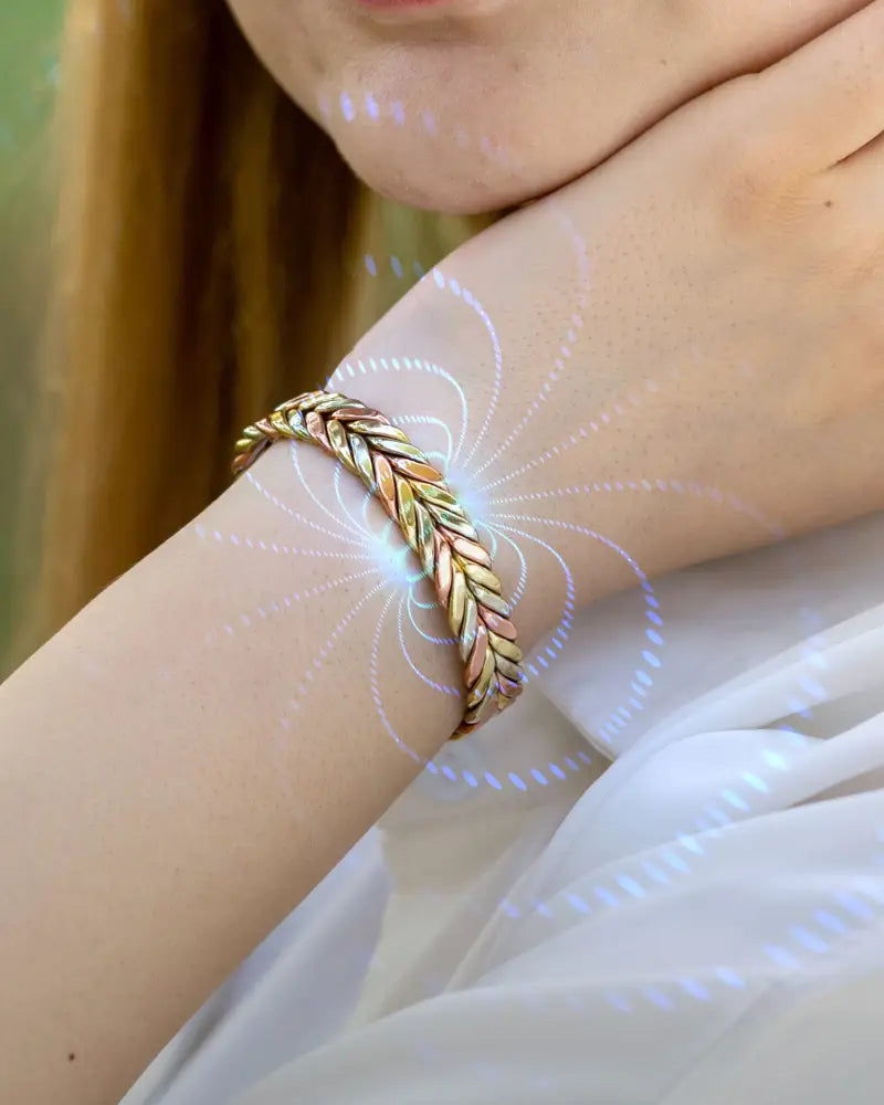 A gold-toned tri-tone magnetic therapy braided copper cuff bracelet with a textured woven design worn on a wrist