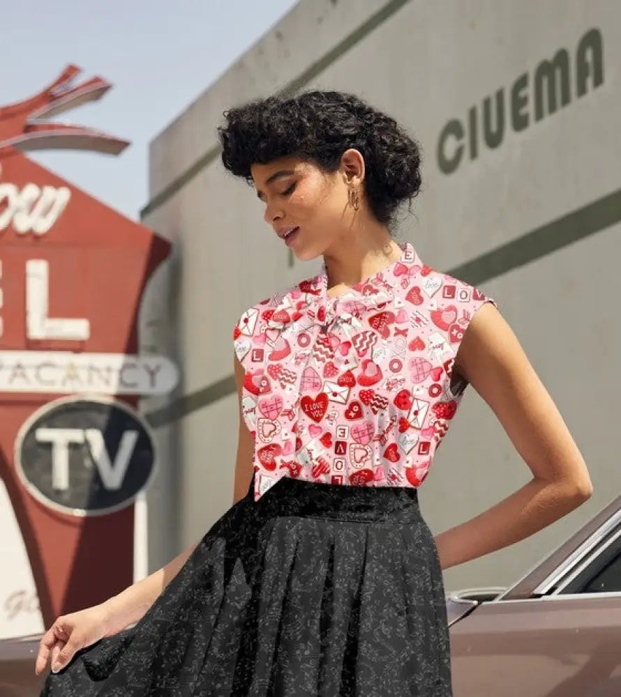 A woman wears a sleeveless high neck vintage 1950s cotton top with playful red and white xoxo print pattern
