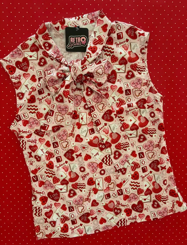 A sleeveless white cotton blouse with a red and pink heart print by retro luciana featuring a bow neck design