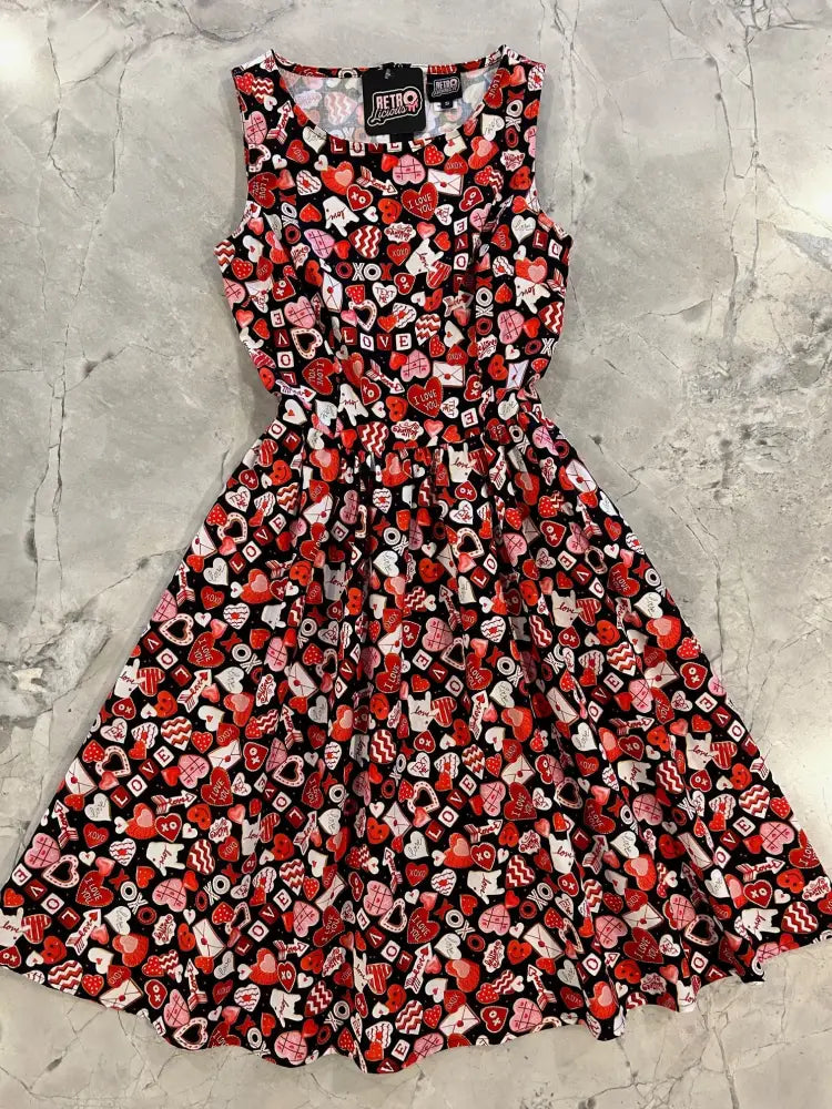 A sleeveless black cotton dress with vibrant red, pink, and white heart and love note vintage 1950s print