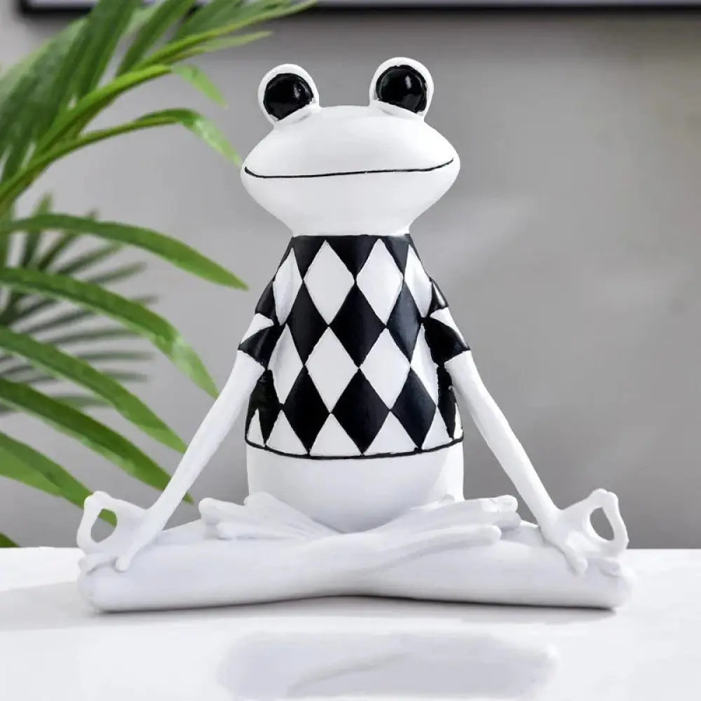 White ceramic frog figurine wearing black and white diamond-patterned vest in a meditative yoga pose