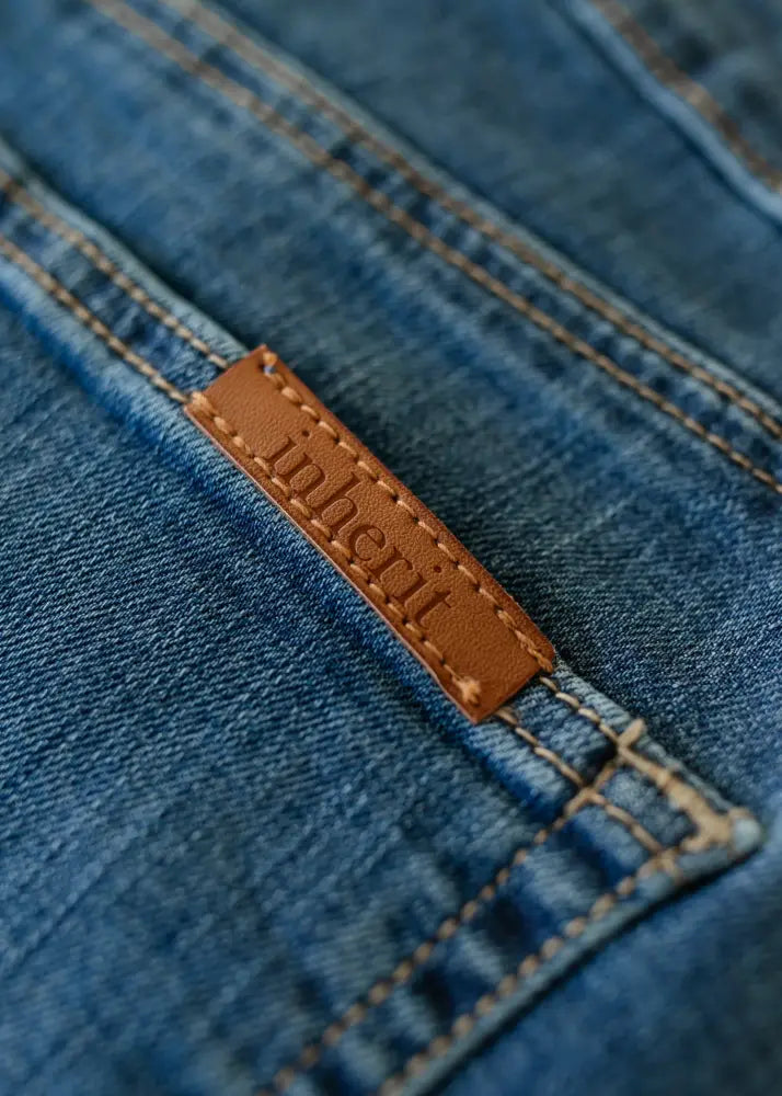 A tan leather brand tag with inheri stitched in dark thread on the back of a medium-wash blue denim zana midi skirt