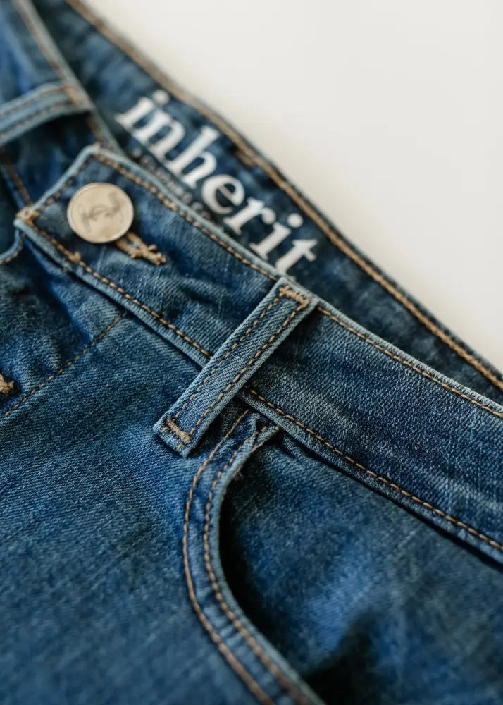 Blue denim midi skirt with front metallic button, kick pleat, and white inherit brand label on waistband