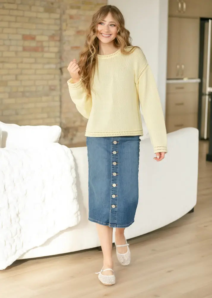 A pale yellow long-sleeved knitted sweater with lace trim paired with a zana front button denim midi skirt with kick pleat