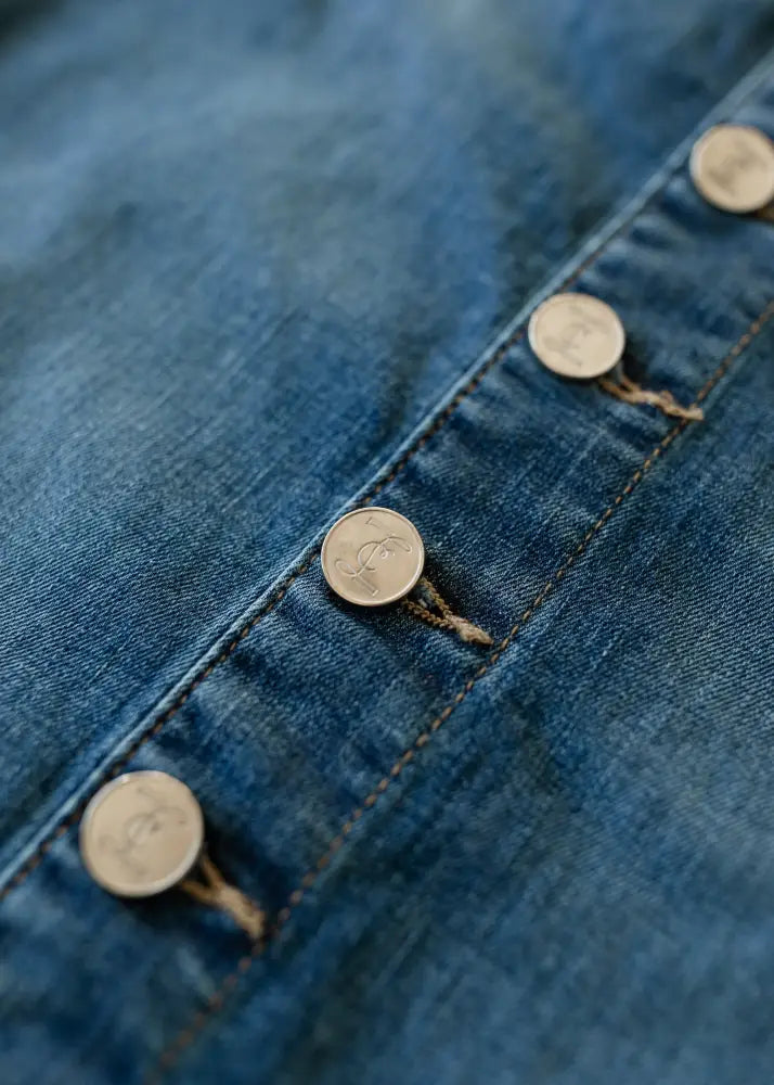 Blue denim fabric with a row of metallic circular embossed buttons on the zana front button denim midi skirt