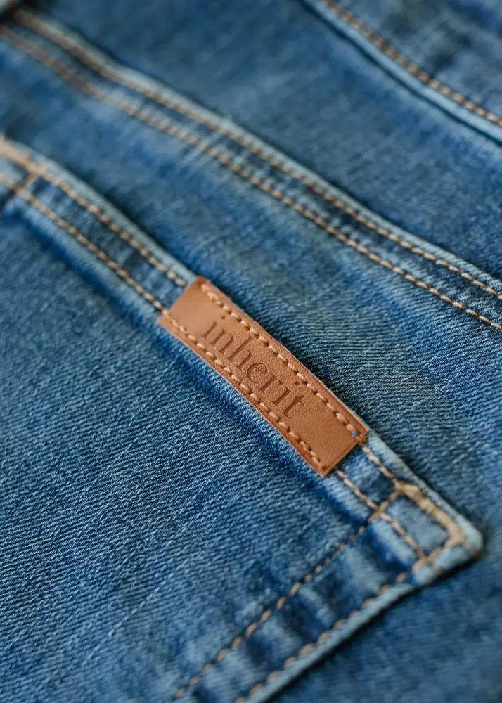 A tan leather inheri brand tag stitched on medium-wash blue denim in the zana front button midi skirt with kick pleat