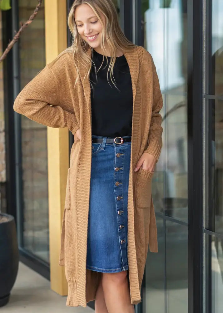 Tan ribbed-knit long cardigan worn over a black top and zana front button denim midi skirt with kick pleat